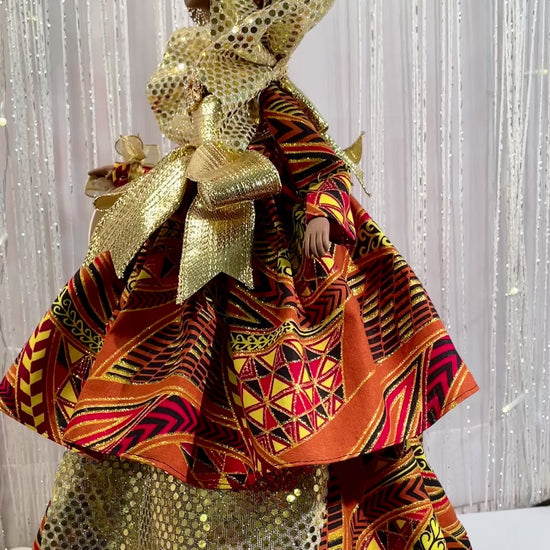 VIDEO OF AN EDUCATED BLACK QUEEN ART DOLL. She is dressed in a two tiered sparkly afrocentric fabric gown. Gold embellishments abound on this Black Queen from the collar to the waist to the draping from under her top tier. This gown is accented with a gold rhinestone cabachon at the bodice. She wears gold rhinestone earrings