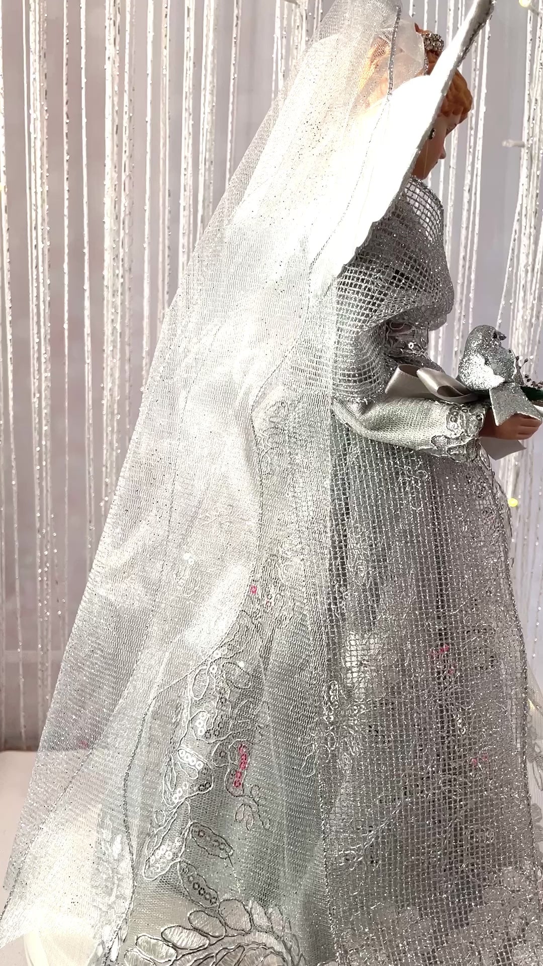 Video of Blonde Christmas Angel dressed in silver gown with silver wings holding a silver bird.